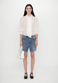 Camicia bianca trasparente con fiocco, pantaloni corti di denim blu, ballerine nere a pois, e una piccola borsa bianca. Design minimalista, stile casual.