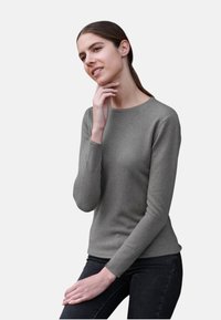 Haut à manches longues gris clair avec un col rond, en tissu lisse, silhouette ajustée, associé à un jean foncé. Design minimaliste.