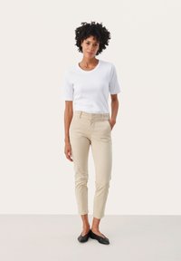 T-shirt bianco a maniche corte, pantaloni beige aderenti e scarpe nere flat. Design semplice e texture liscia con una silhouette classica.
