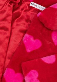 Czerwony materiał z futra ekologicznego z różowymi wzorami serc, z gładką czerwoną satynową podszewką. Zawiera białą metkę z napisem "minoti".