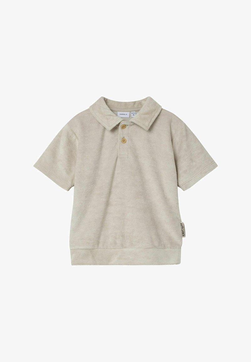 Beige lühikese varrukaga polosärk, mis on valmistatud pehmest ja tekstureeritud kangast, millel on krae, kolme nupuga läbilõige ja väike silt küljel.