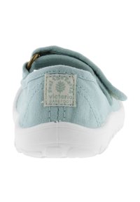 Zapatilla slip-on de lona azul claro con suela de goma blanca y una etiqueta con el logo en la parte trasera. Textura suave y detalles de diseño minimalistas.