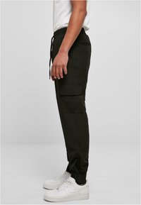 Donker cargo pantalons met een elastische tailleband, zijzakken en taps toelopende pijpen, gecombineerd met witte sneakers. Soepele, gestructureerde stof.