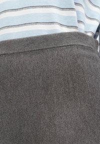 Grauer Strickstoff mit glatter Textur, der oben am Bund teilweise ein blau-weiß gestreiftes Oberteil zeigt.