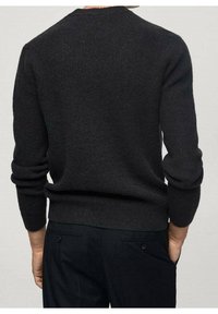 Schwarzer Strickpullover mit rundem Halsausschnitt, gerippten Bündchen und Saum, mit einer strukturierten Verarbeitung. Getragen mit maßgeschneiderten dunklen Hosen.