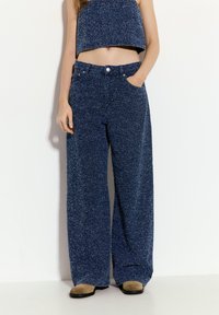 Kalhoty s vysokým pasem a širokými nohavicemi z texturované námořnické tkaniny. Mají přední kapsy a zapínání na knoflík. V kombinaci s odpovídajícím zkráceným topem.