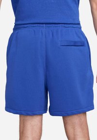 Blå träningsshorts i mjukt tyg med elastisk midjeband, sidofickor och en platt fåll. Har en enkel, sömlös design.