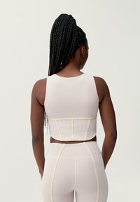 Světle růžový sportovní crop top s přiléhavým designem, jemnou texturou a žlutými akcentovými švy. Nosený s odpovídajícími legíny s vysokým pasem.