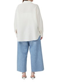 Witte, gestructureerde, langoe mouw hem met een kraag, gecombineerd met lichtblauwe, wijde jeans en witte, gespenhakken.