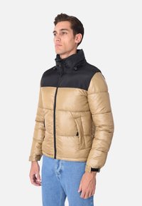 Giacca imbottita caratterizzata da un corpo color sabbia con colletto nero, chiusura con zip e tasche laterali; realizzata in un materiale lucido e leggero.