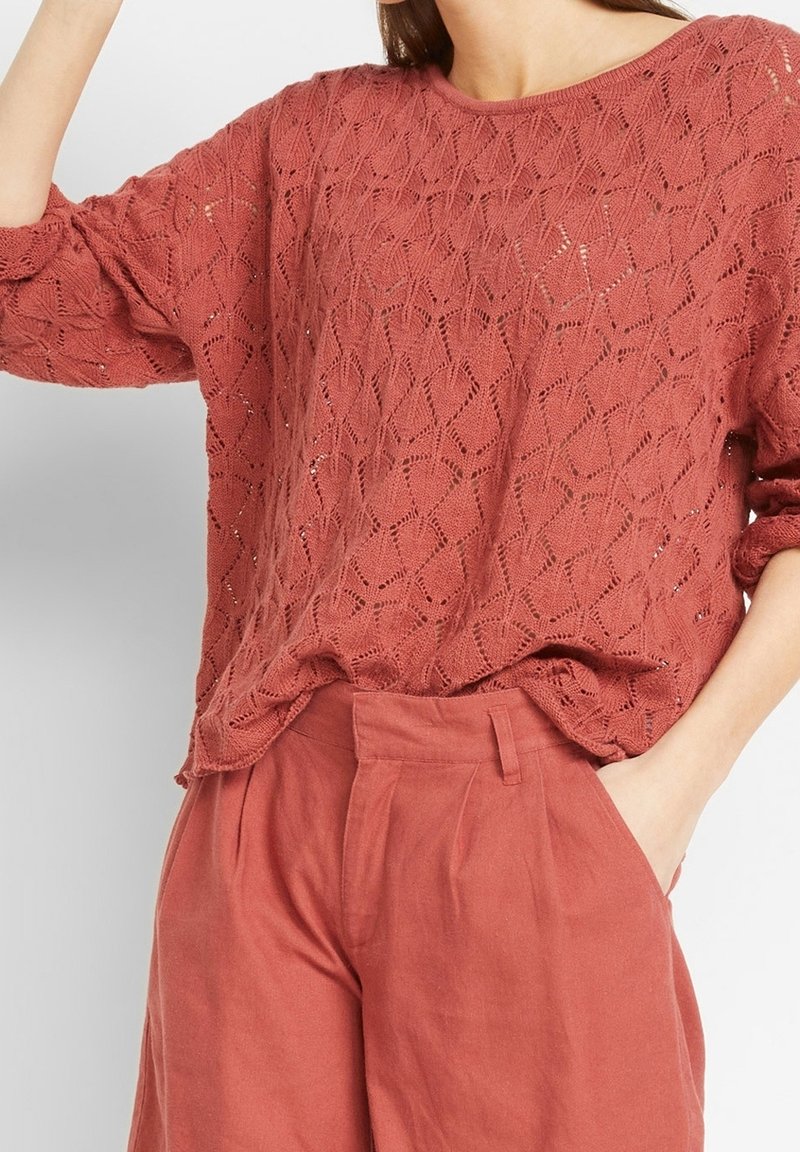 Top de punto suelto en rosa empolvado con un patrón de diamantes, cuello redondo y mangas largas, acompañado de unos pantalones holgados a juego.