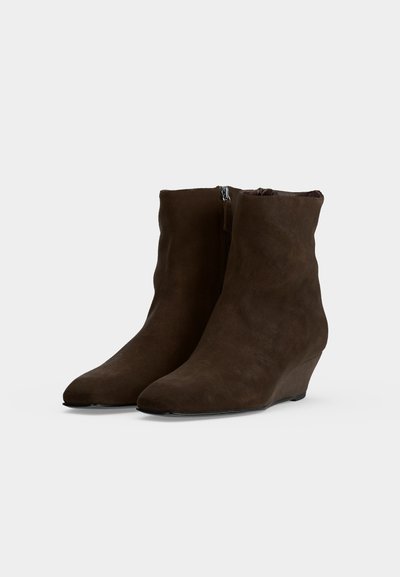 Paire de bottines en daim marron foncé avec talons compensés et fermetures éclair latérales, affichée sur un fond clair uni.