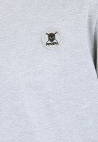 Sudadera gris con un parche bordado circular que presenta un diseño de calavera y huesos cruzados, delineado en beige. Tejido suave y texturizado.