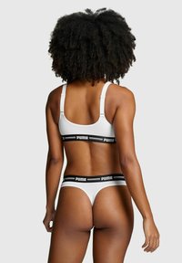 Weißes Sport-BH- und Tanga-Set mit einem schwarzen PUMA-Logo auf dem elastischen Band, verstellbaren Trägern und einer glatten Textur.