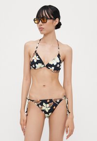 Set bikini floreale con sfondo nero, design a colletto halter e lacci laterali regolabili sul fondo. Texture opaca con dettagli colorati.