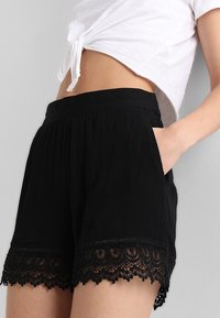 Czarne szorty z teksturowanej tkaniny, elastycznym paskiem w talii i koronkowym wykończeniem u dołu. Zawierają boczne kieszenie dla większej wygody.