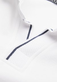 Vitt polo-shirt med en texturerad tygkvalitet och en mörk marinrand som löper vertikalt i kragen och över framsidan.