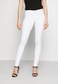 Jeans skinny brancos feitos de denim, com um design ajustado, estilo de cinco bolsos e uma textura suave. Combinados com sandálias de salto alto pretas.