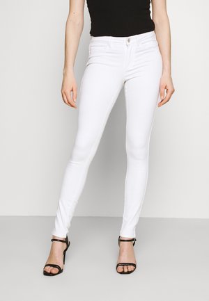 Jeans skinny brancos feitos de denim, com um design ajustado, estilo de cinco bolsos e uma textura suave. Combinados com sandálias de salto alto pretas.