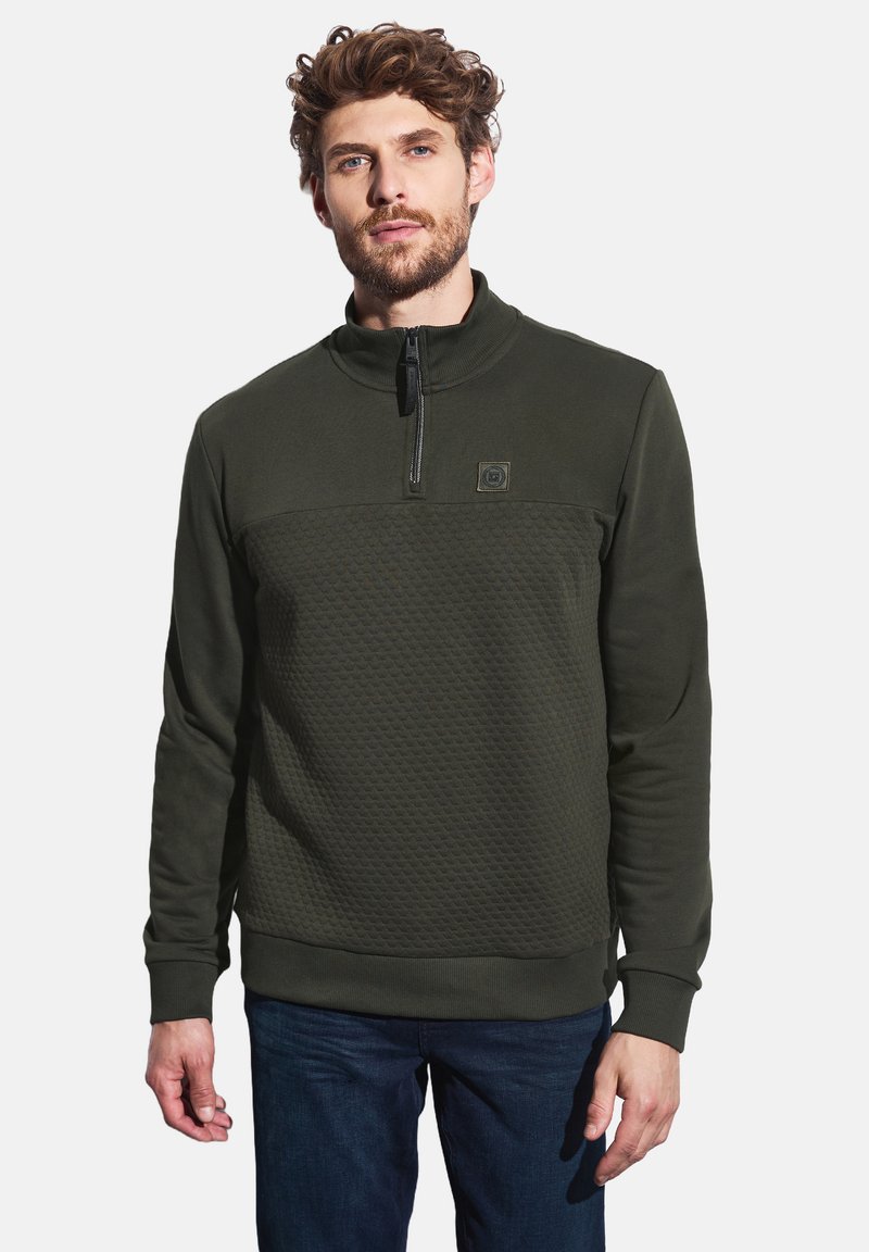 Zelená mikina na zip, která má texturovanou panel přes hrudník, pružné manžety a stojáček. Měkký povrch látky.