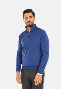 Maglione a mezza zip blu realizzato in tessuto morbido. Presenta polsini e orlo a costine, con un colletto bianco a contrasto sottostante.