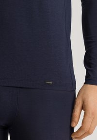 Marineblauw longsleeve shirt van zachte stof. Heeft een slim fit en een klein Hanro-logo label dicht bij de zoom. Naaddetails zijn zichtbaar.