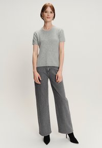 Grijze gebreide top met korte mouwen, gecombineerd met hoogsluitende zwarte wijde jeans, aangevuld met zwarte puntige hakken.