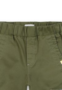 Olijfgroene shorts met een elastische tailleband, witte stiksels, twee opgestikte zakken aan de voorkant en een gele accenttag aan de zijkant.