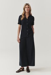 Camisa de botones navy con mangas remangadas, combinada con pantalones anchos navy y sandalias oscuras. Textura de tela suave con un ajuste relajado.