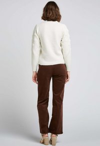Pull blanc avec des accents en pompons texturés sur les manches, associé à un pantalon en velours côtelé marron et des talons beiges à lanières, vu de dos.