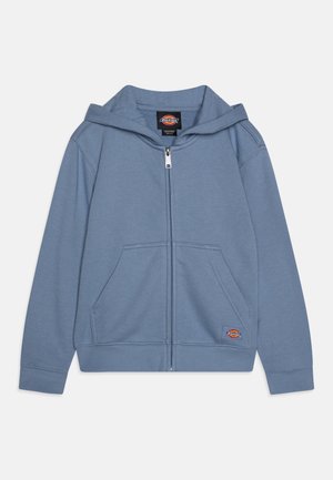 Lyseblå hettegenser med glidelås laget av mykt materiale, med en frontlomme, ribbede mansjetter og en logopatch på nedre venstre side.