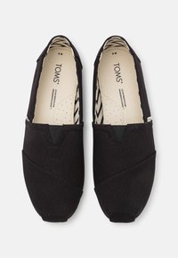 Mustad musta kangast slip-on kingad, millel on elastsed sisenemised, ümar varvas ja mustriline tekstiilvooder, millel on sakilise mustriga disain.