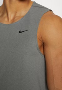 Graues ärmelloses Sportoberteil mit rundem Ausschnitt. Hergestellt aus einem strukturierten Stoff und mit einem schwarzen Nike-Logo auf der Brust.