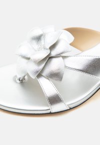 Ασημένιο σανδάλι με μεγάλο μεταλλικό λουλούδι διακοσμητικό στο λουράκι και στρογγυλεμένο σχέδιο μύτης.