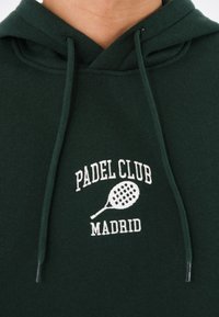 Hanorac verde din bumbac, cu șnur, având brodat în alb textul "PADL CLUB MADRID" și un grafic cu o rachetă de tenis.