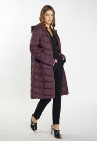 Dlhý, nadýchaný kabát v tmavofialovej farbe so zapínaním na zips a kapucňou. Obsahuje horizontálne prešívanie a zlatý zips, skombinovaný s čiernymi nohavicami na mieru a lodičkami.