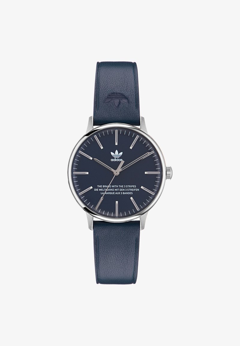 Vīriešu pulksteņa apaļa sudraba nerūsējošā tērauda korpuss, tumši zils ādas siksniņa, minimālisma skaitītājs, sudraba stunda atzīmes un Adidas logo.