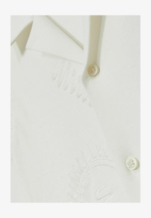 Valge särk, millel on nööplukk ja peenelt brodeeritud detailid. Kangas tundub pehme, ühtlase tekstuuriga ning klassikalise krae kujundusega.