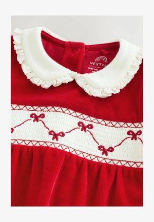 Raudona suknelė su balta rauktine apykakle, išsiuvinėtų kaspinų ant balto skydo ir tekstūrinio audinio. Mygtukų užsegimas nugaros pusėje.