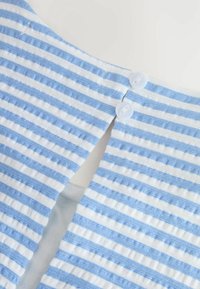Gros plan sur un tissu rayé bleu et blanc avec deux boutons blancs attachés à une ouverture fendue.