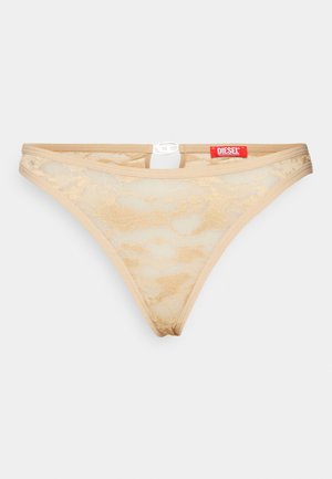 Fio dental bege em rendas com uma textura transparente, apresentando um pequeno detalhe recortado na parte de trás e um rótulo da marca Diesel em vermelho na cintura.