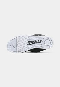 Schwarz-weiße Sneaker-Sohle mit geometrischem Profil und dem in Schwarz auf der weißen Sohle aufgedruckten "ETNIES"-Logo.