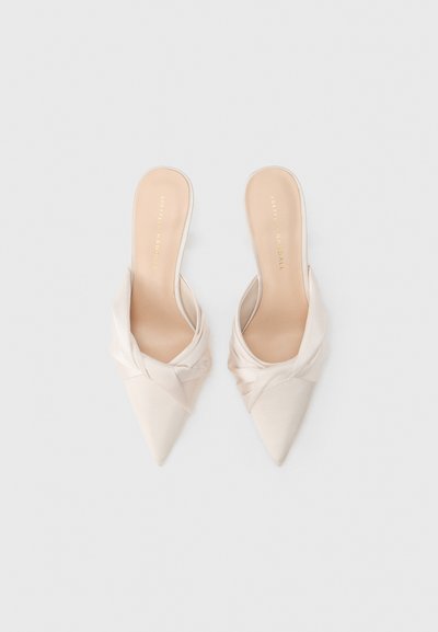 Mules à bout pointu en satin beige pâle avec un design supérieur noué. Texture lisse et dos ouvert créent une silhouette élégante.