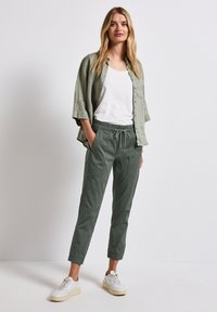 Ljusgrön linne skjorta över en vit tanktop, tillsammans med mörkgröna byxor med elasticitet i midjan som har två framfickor och vita sneakers.