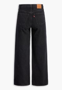 Jean noir à jambes larges vu de dos avec deux poches, un patch en cuir marron de la marque, et une petite étiquette en tissu rouge sur la poche droite.