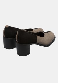 Chaussures à talon bloc grises et noires en daim avec un bout arrondi et un design découpé, présentant une texture lisse et un contraste de couleurs distinct.