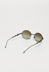 Ochelari de soare negri cu lentile rotunde, nuanță gradient întunecată, brațe metalice ondulate și suporturi pentru nas. Design minimalist pe un fundal alb.