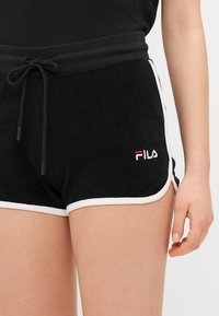 Melnas frotēta auduma šorti ar baltu apdari, ar elastīgu jostasvietu, aukliņu un sarkanu un baltu FILA logo uz kreisā kājas.