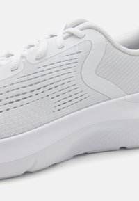 Chaussure de sport blanche avec une tige en maille, des motifs texturés et une semelle en caoutchouc épaisse. Présente des lacets plats et des détails subtils sur le côté.