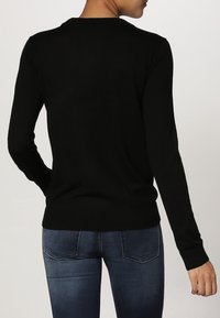 Black long-sleeve sweater with a crew neck, made of textured fabric, fitted silhouette, and ribbed cuffs. Paired with dark blue jeans.